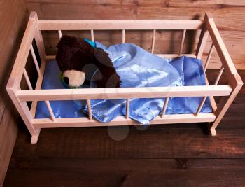 Cute teddy bear sleeping in wooden bed in his room