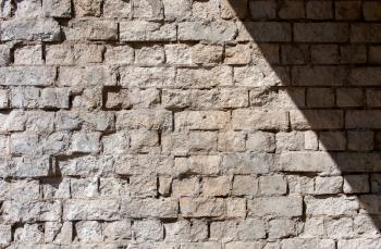 an old wall of white cracked brick with fallen off plaster and a diagonal shadow in the right corner