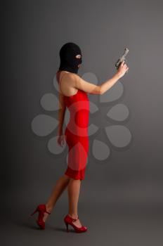 sexy girl in tight bright red dress and balaclava holds automatic pistol in hand on a dark background