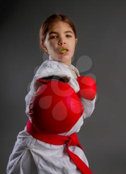 A little girl karateka in white kimono and in a red belt with a mouth guard in her lips should be ready for the fight