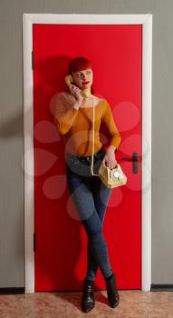 Pretty woman talking on an old dial telephone with a twisted wire on the background of a bright red door