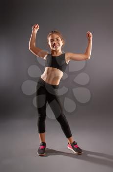 little girl in sportswear doing gymnastics and posing against a dark background