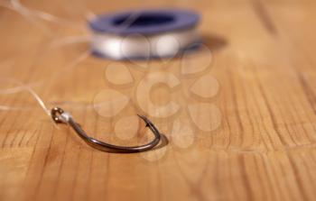 Large classic fishing hook with a thin fishing line tied to it in a reel on a wooden background