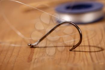 Large classic fishing hook with a thin fishing line tied to it in a reel on a wooden background