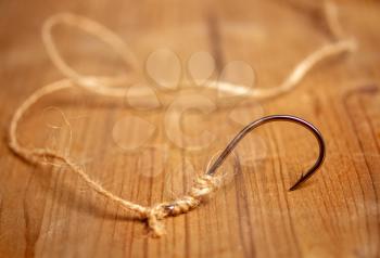 Large classic fishing hook with a coarse rope tied to it on a wooden background