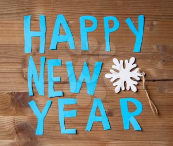 Happy New Year inscription casually cut out by scissors from blue paper laid out on a wooden background