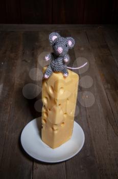 a small toy mouse the symbol of 2020 sits on a large piece of cheese with holes in a dark room