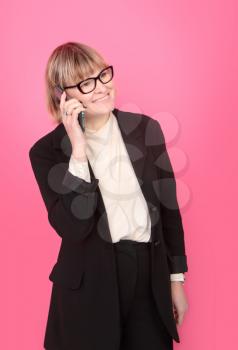 business woman in a formal suit happily talking on the phone on a pink background
