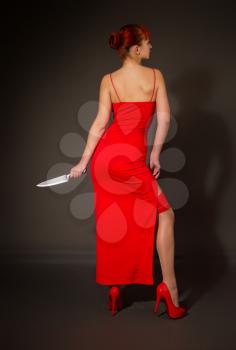 Elegant girl in a red evening dress holds in her hand a large sharp steel kitchen knife for self-defense