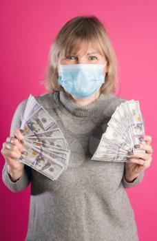 Adult woman in protective medical mask rejoices in sudden wealth or gain against bright pink background