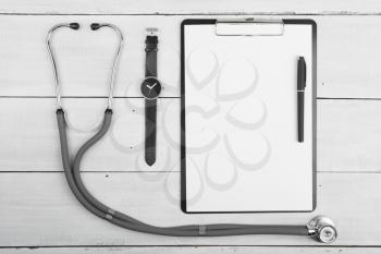 Workplace of doctor - stethoscope, medicine clipboard and watches on wooden desk
