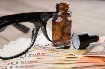 eye care concept - reading glasses, eye drops and money on the wooden desk