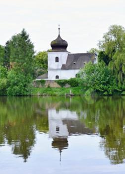Nice small white Church of St. Nicholas in Zisov, Czech Republic. The church is near pond and placed in the beautiful park with old trees.