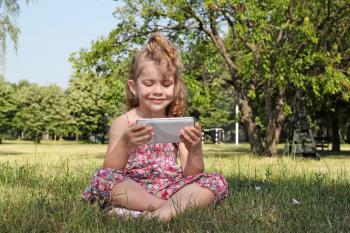 little girl sitting in park and play with tablet pc
