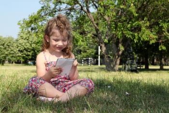 little girl sitting on grass and play with tablet pc