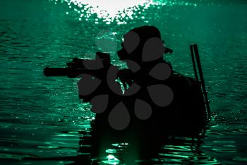 Silhouette of special forces with rifle in action during night raid crossing river in the jungle waist deep in the water. Moon path glowing