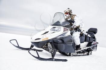 Army soldier in winter camo somewhere in the Arctic moving across the snow field riding tracked snowmobile