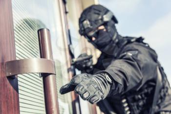 Police special security operations group fighter, SWAT team member in black uniform, armed with pistol reaching hand to grab door handle before break into building during security operation, close up