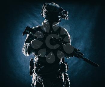 Equipped modern ammunition, armed assault rifle with silencer, standing in darkness with four lenses night vision goggles on battle helmet commando soldier low key, studio portrait on black background