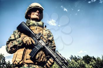 Location shot of United States Marine with rifle weapons in uniforms. Military equipment, army helmet, warpaint, smoked dirty face, tactical gloves. Weapons, army, patriotism concept