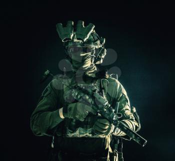 Half length, low key portrait of elite commando fighter, professional mercenary hiding identity behind mask, glasses, standing in darkness with mini submachine gun in hands, wearing nigh-vision device