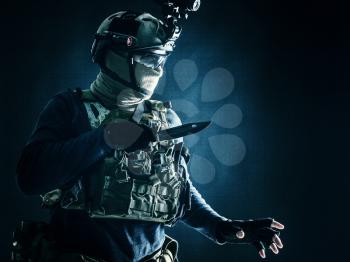 Special operations soldier, commando fighter, modern warfare combatant in combat uniform, helmet with night-vision, wearing mask and glasses, sneaking in darkness for sentry quiet removal with knife