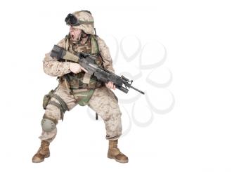 Studio shoot of modern infantry soldier, U.S. marine rifleman in combat uniform, helmet and body armor, screaming and crouching down with assault service rifle in hands isolated on white background