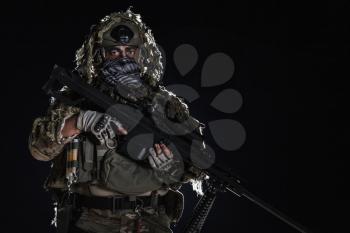 Army sniper with big rifle standing on black background. Face is painted with warpaint. Backlit contour silhouette shot