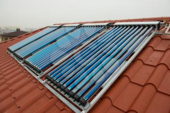 Vacuum collectors- solar water heating system on red roof of the house.
