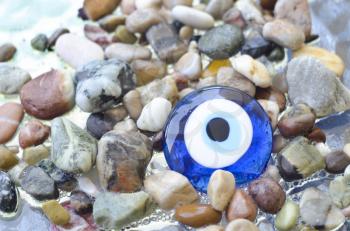 Colorful pebbles on the beach with turkish evil eye glass bead. Background with color stones on the sea and amulet. Sea shore bright stones, pebble, gravel, boulder,