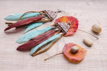 Handmade earrings with author's ceramics and colored feathers.Composition with stones and leaves on a light wooden background ..