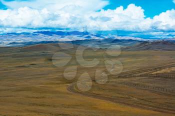 Road stretches into the distance across the steppe, mountains, blue sky with clouds. Chuya Steppe  in the Siberian Altai Mountains, Russia