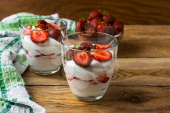 Layered strawberries dessert with cream cheese on rustic wooden background. Whipped cream with fresh strawberry.