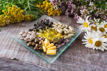 Ayurvedic herbal pills on the glass plate and wild chamomile, tansy, oregano. Healthy life concept