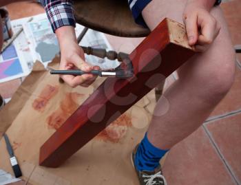 Holding and painting wooden table leg. Painting brush in hand. DIY or do it yourself concept with painting wood. Home improvements and renovation of wooden furniture.