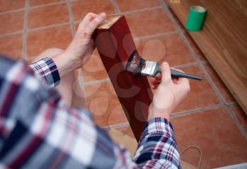 Closeup view of home renovating and old furniture painting. Man holds painting brush and paints wooden board.  Top view of hands holding painting brush