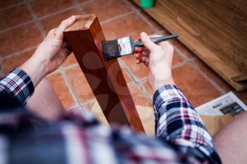 Man holds painting brush and paints wooden board. Closeup view of home renovating and old furniture painting.  Top view of hands holding painting brush