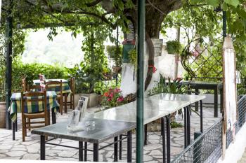 Paleokastritsa, Cofru, Greece- MAY 10, 2018 Inside looks of Taverna the greek restaurant with tables and chairs with the garden. restaurants is set for a smaller group people
