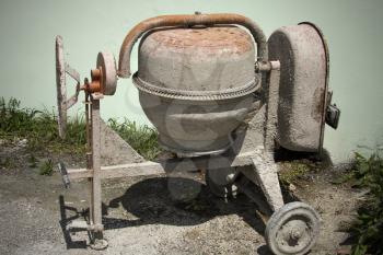 Rarely used Cement mixer standing near wall. Cement mixers, or concrete mixers, allow users to mix large amount of cement, sand, or gravel with water.