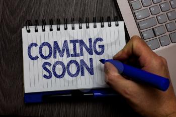 Writing note showing Coming Soon. Business photo showcasing something is going to happen in really short time of period Man holding marker spiral notebook computer keyboard wooden background