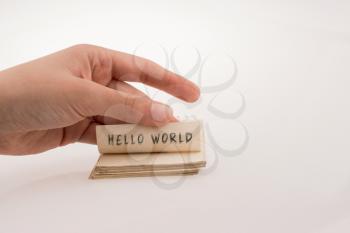 Hand holding notebook page with HELLO WORLD wording on white
