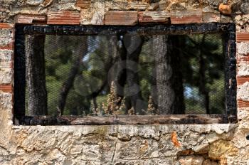Burned wooden window frame with view to a forest and old brick wall background.