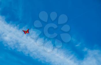 A kite that resembles a butterfly hovers in the blue sky.