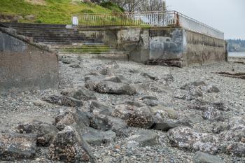 Low tide in West Seattle, Washington reveals a rugged seabed leading up to a cement stariway that is built in to a seawall.
