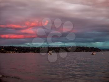 Two boats are anchored at Three Tree Point, Washington as the sun sets.  A pink and purple sky blankets the Puget Soiund.