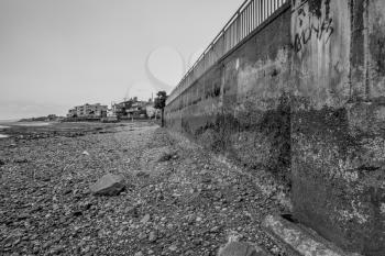 The tide is out on the West Seattle, Washington shoreline. A seawall and the seabed are uncovered revealing a rugged terrain. Black and white image.