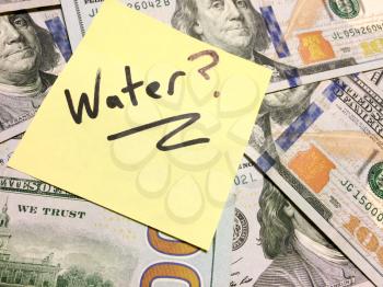 American cash money and yellow post it note with text Water with question mark in black color aerial view