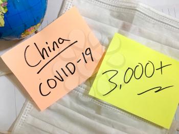Coronavirus COVID-19 China infection medical cases and deaths. COVID respiratory disease influenza virus statistics hand written on surgical mask and earth globe background