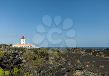 White lighthouse built on volcanic rocks with blue sky background at Pico Island, Azores