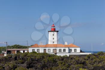 White lighthouse built on volcanic rocks with blue sky background at Pico Island, Azores